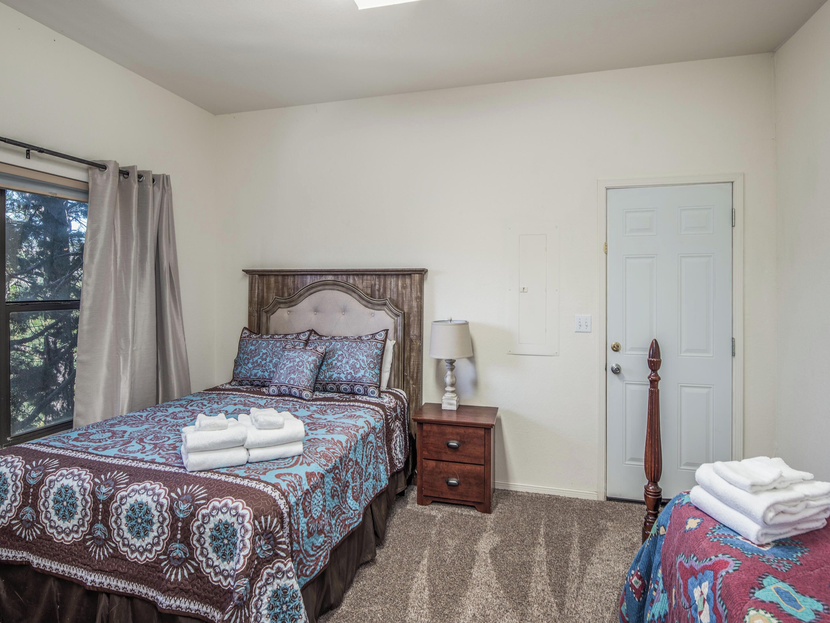 A bedroom with a bed, a nightstand, a lamp, a door, and a window with curtains.