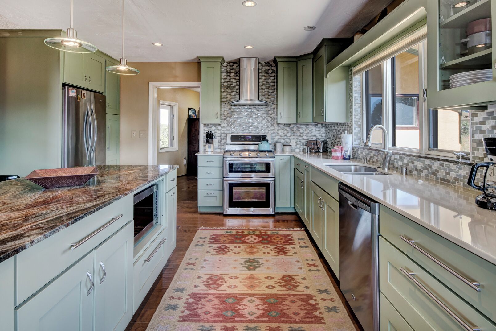 A modern kitchen with green cabinets, stainless steel appliances, and a patterned rug.