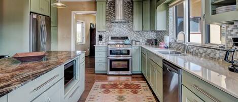 A modern kitchen with green cabinets, stainless steel appliances, and a patterned rug.