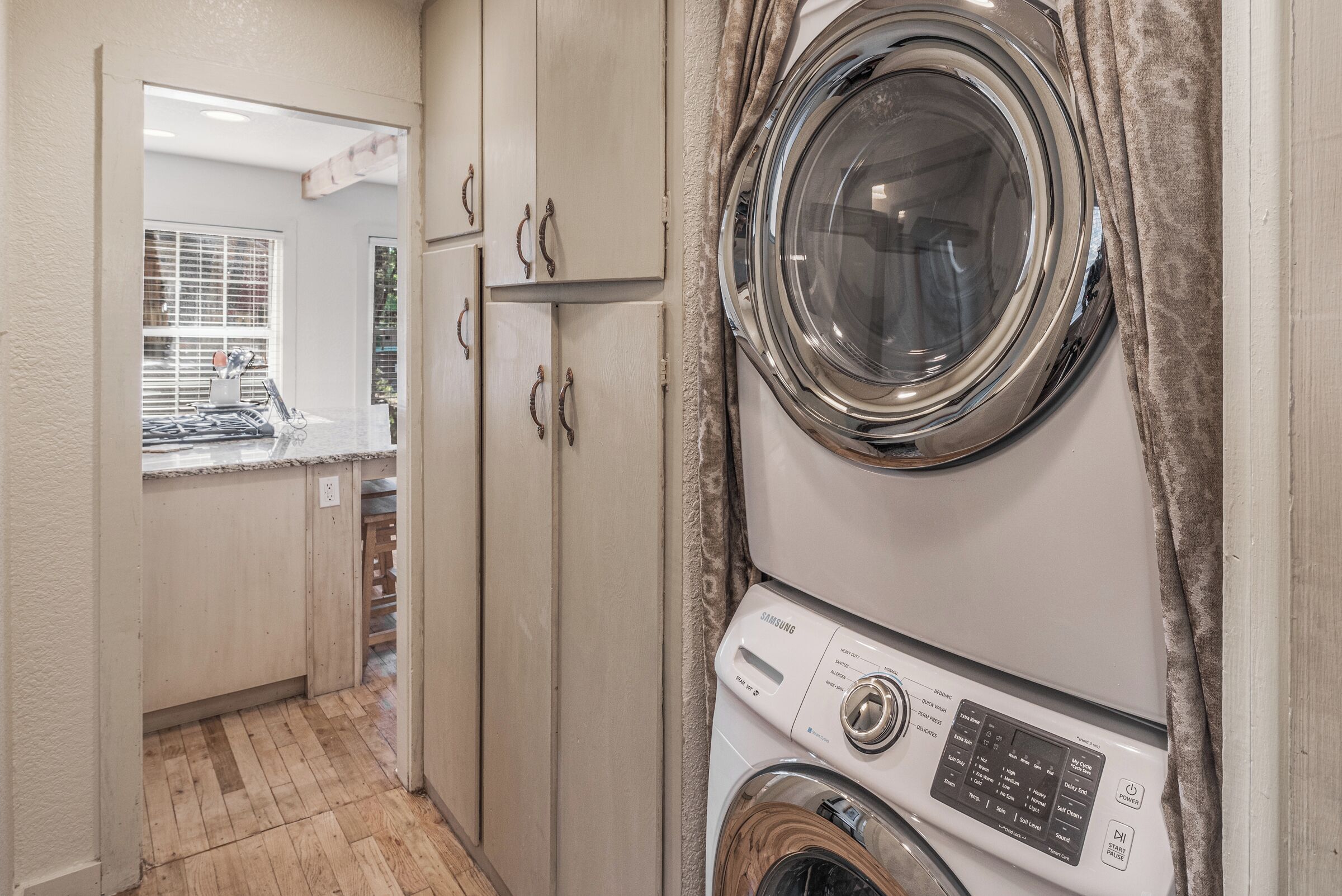 Une buanderie équipée d’un lave-linge et d’un sèche-linge, de meubles en bois et d’une fenêtre avec des stores.