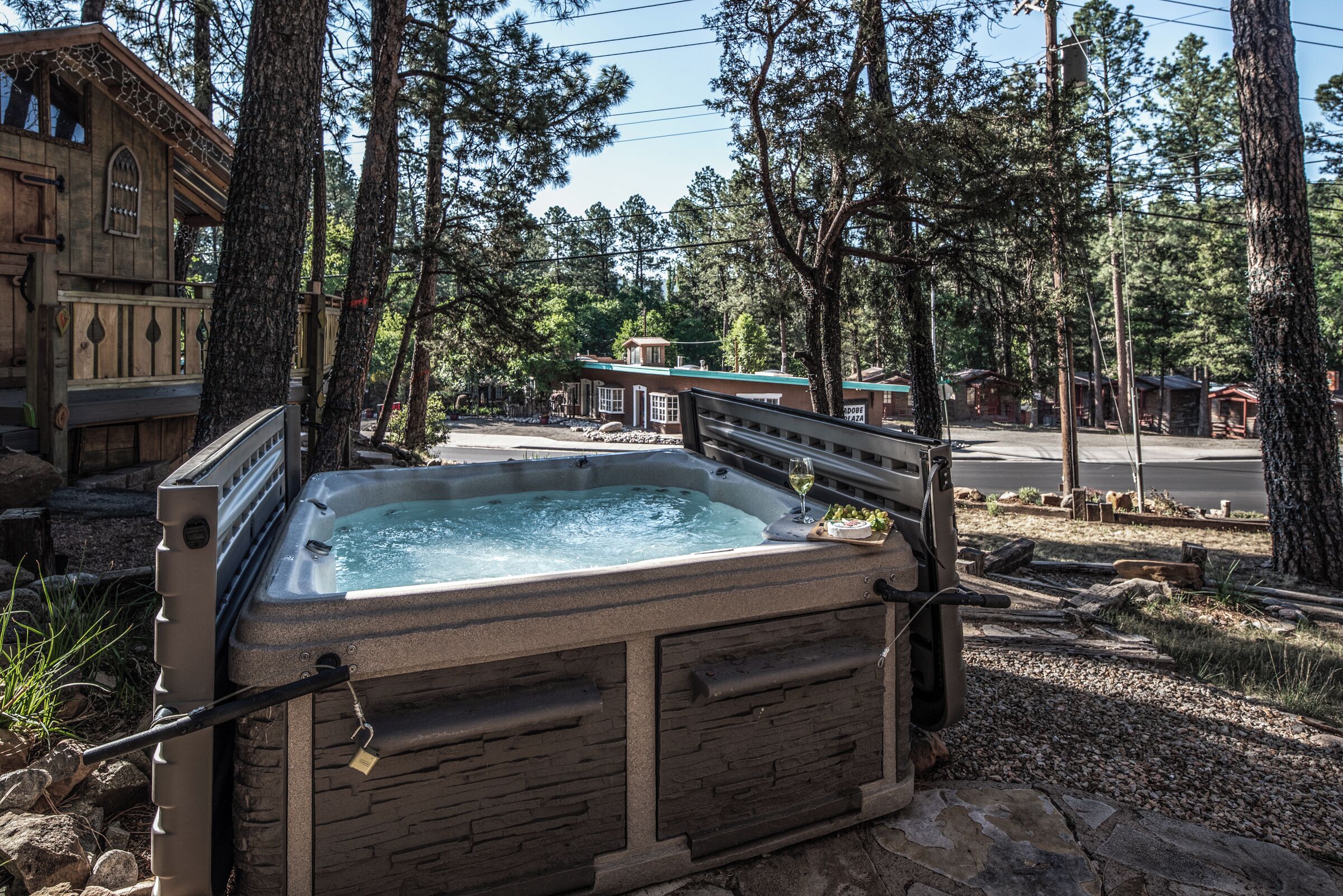 A hot tub in a wooded area with a stone exterior, surrounded by trees and a small building in the background.