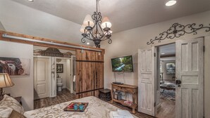 A bedroom with a large bed, a chandelier, a television, and a wooden wardrobe. - Sugar Butter Chalet by Ruidoso Vacation Rentals (Ruidoso)