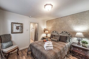 Une chambre à coucher avec un grand lit, une chaise, une table de chevet et une lampe fixée au mur.