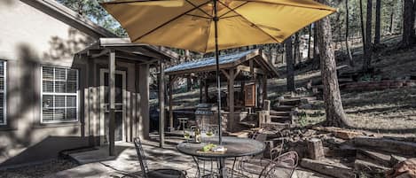 An outdoor patio with stone flooring, a round table, metal chairs, and a large yellow umbrella.