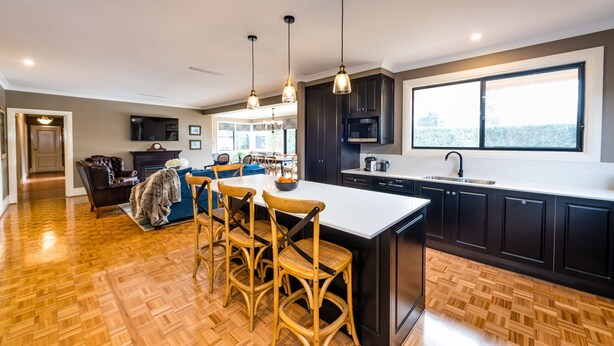 Una cocina moderna con una isla central, muebles oscuros e iluminación colgante.