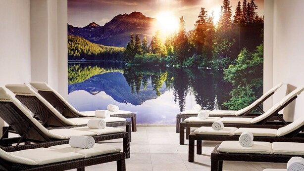 Een wellnessruimte met ligstoelen, een groot wanddecor van een meer en bergen, en een plafond met inbouwspots.