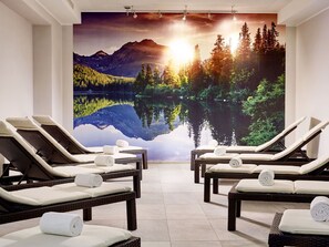 A spa room with reclining chairs, a large wall mural of a lake and mountains, and a ceiling with recessed lighting.