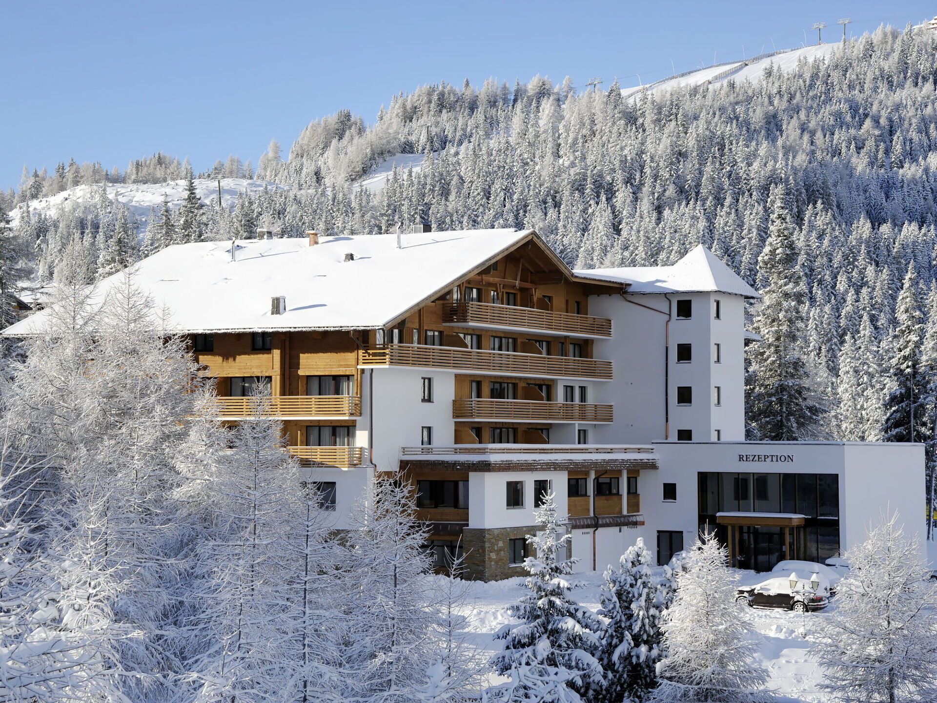 A multi-story hotel with a reception area, wooden balconies, and a view of snow-covered trees and mountains.