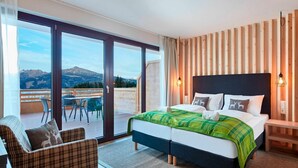 Een slaapkamer met een bed, een stoel, een nachtkastje en uitzicht op bergen door een schuifdeur.