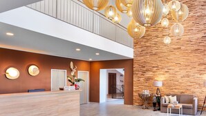Een moderne hotellobby met een houten receptiebalie, een trap en een zithoek met een bank en salontafel.