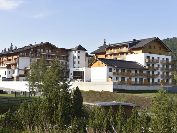 A multi-story hotel with a reception area, balconies, and a mountainous backdrop.