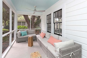 A covered porch with wicker furniture, a ceiling fan, and large windows.