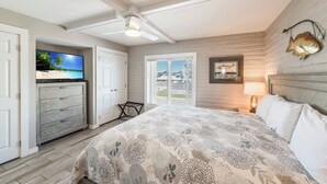 Une chambre à coucher avec un lit, un ventilateur de plafond, une télévision et une fenêtre avec des stores.