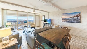 Un vaste espace de vie comprenant une grande table à manger en bois, des sièges confortables, un téléviseur et une vue panoramique grâce à de grandes fenêtres.