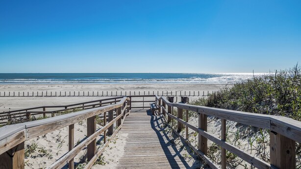 Une promenade en bois qui mène à une plage, avec un ciel bleu dégagé.