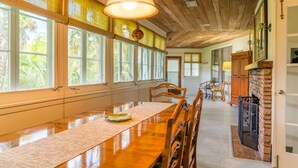 Une longue table à manger entourée de chaises, un plafond en bois et une cheminée en briques.