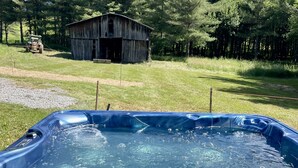 Een hottub in een achtertuin met een houten hut en een tractor op de achtergrond.