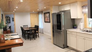 Een moderne keuken met houten plafond, een roestvrijstalen koelkast, witte kasten, en een eethoek met een tafel en stoelen.