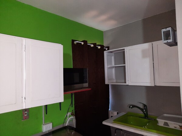 A kitchen with white cabinets, a green sink, and a microwave.