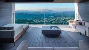 A modern balcony with a wooden floor, two sofas, a coffee table, and a view of a forested landscape.