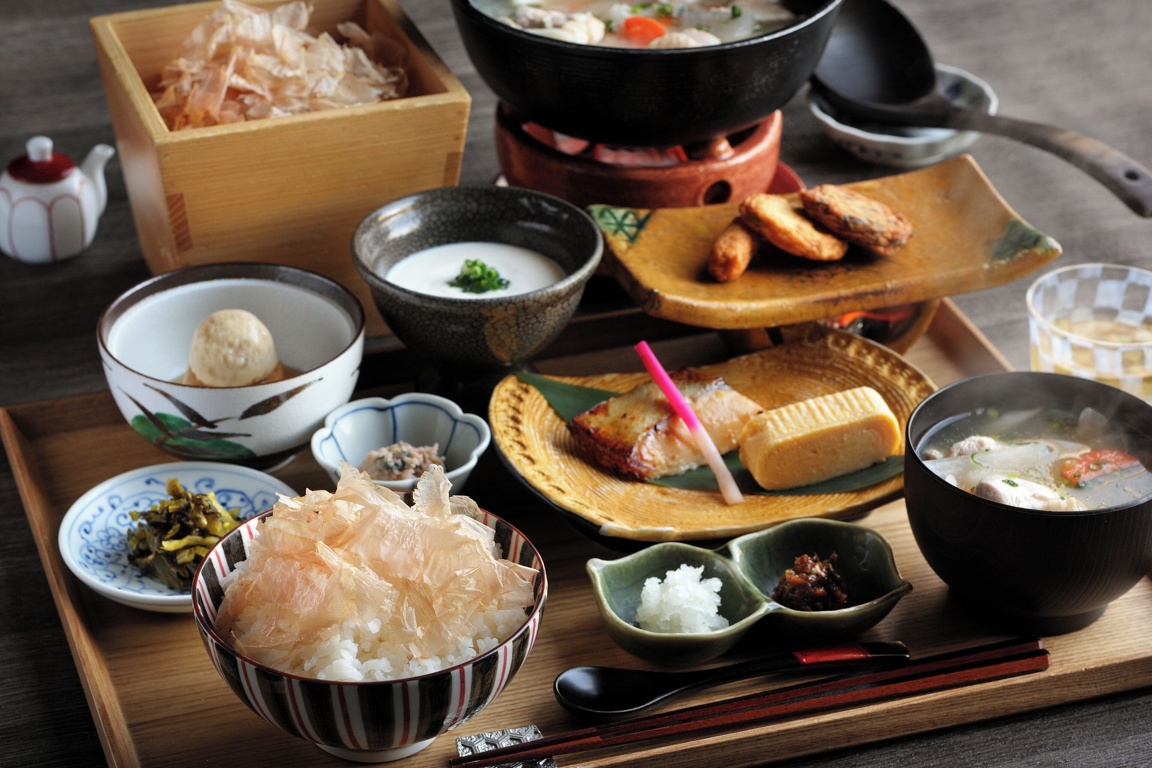 A wooden tray with various Japanese dishes including a bowl of rice, a bowl of soup, and a plate with grilled fish.