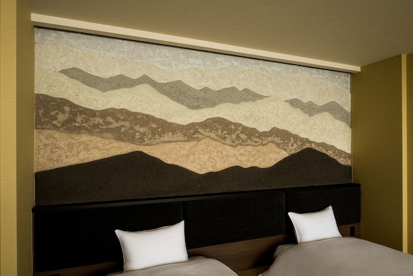Une chambre d’hôtel avec une grande fresque murale représentant des montagnes, une tête de lit sombre et deux lits avec des oreillers blancs.