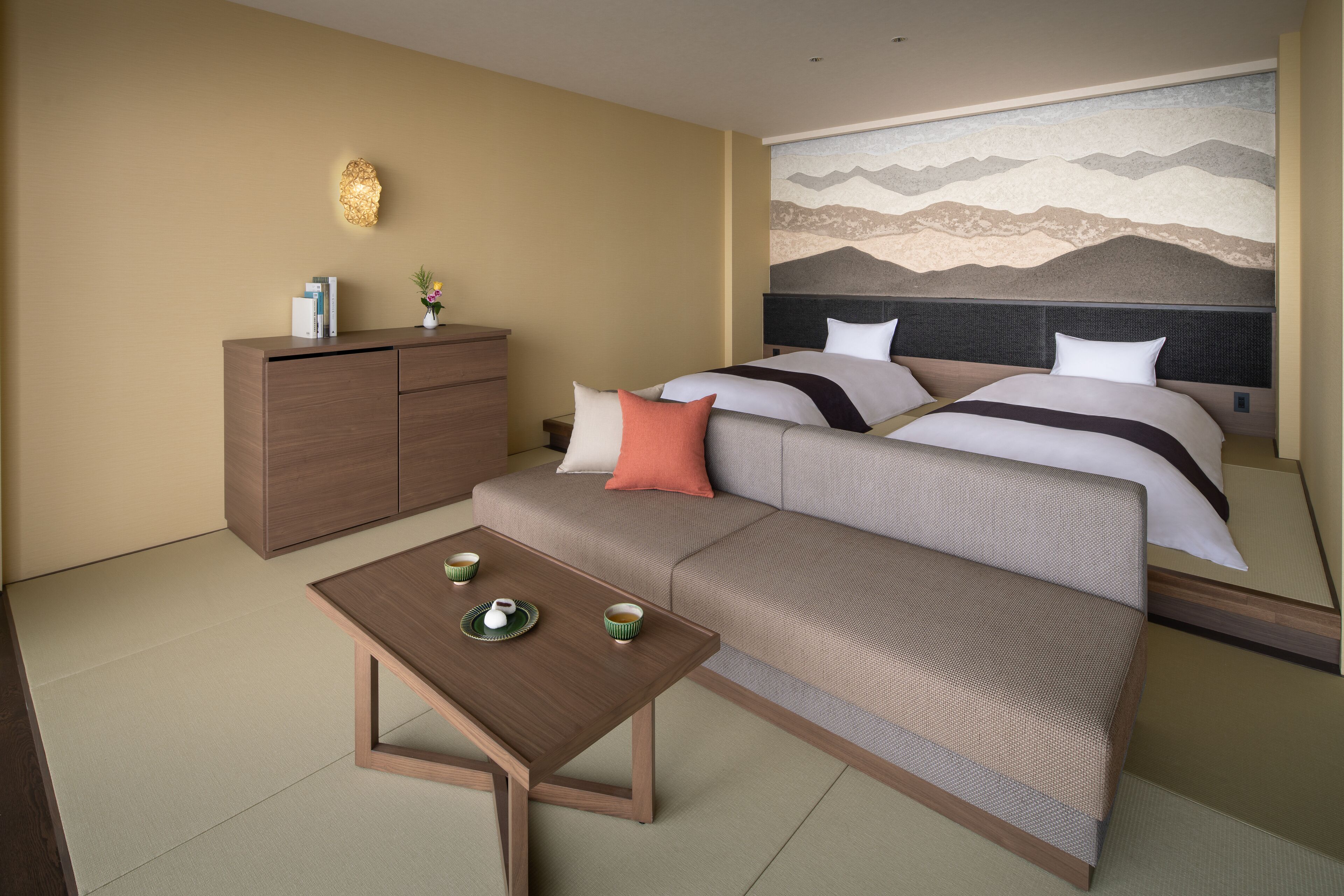 A hotel room with a sofa bed, a small table with tea set, a cabinet, and a wall mural.