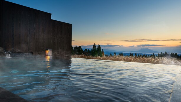 An infinity pool with a wooden structure on one side and a view of trees and mountains in the background.