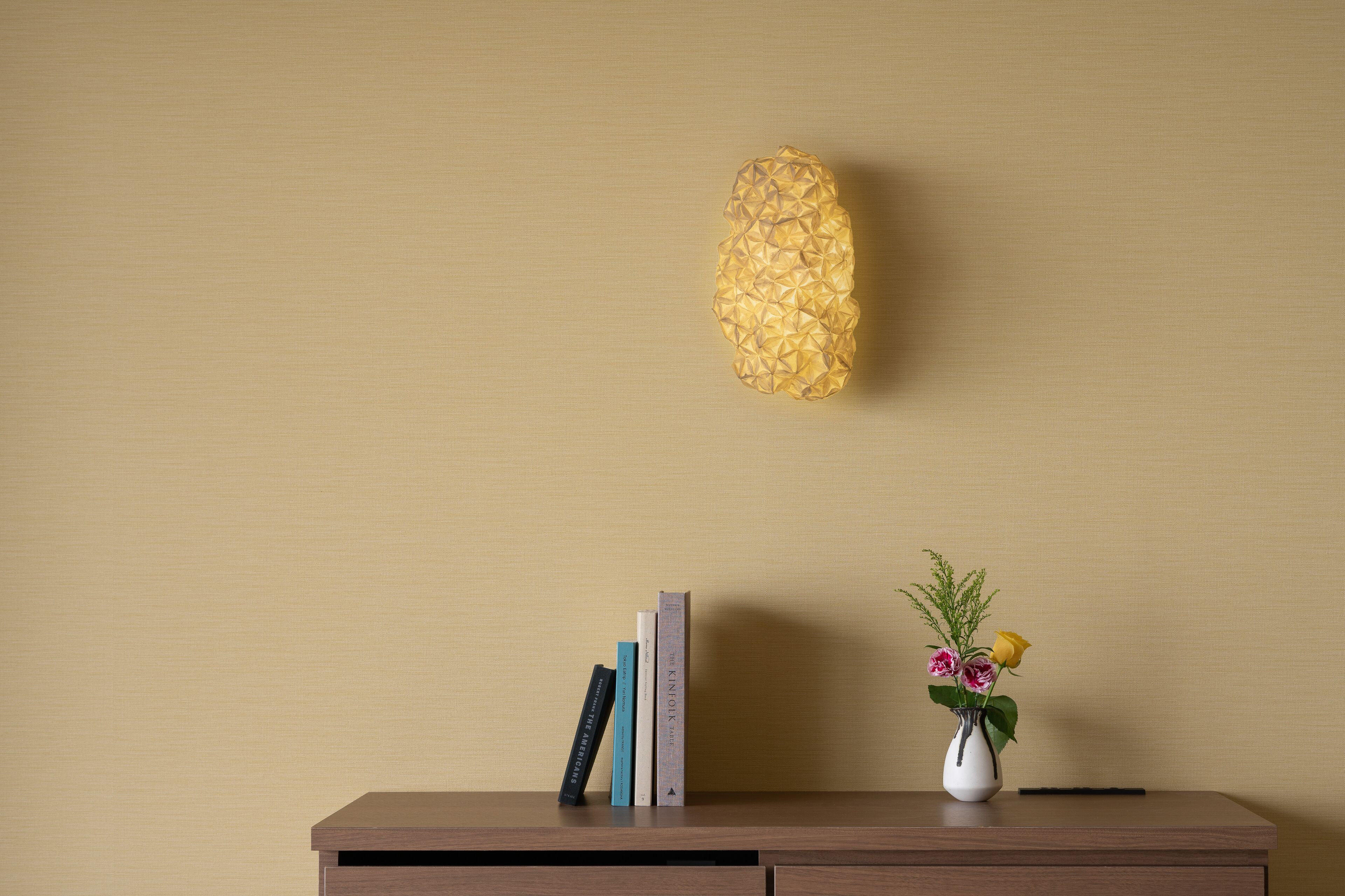 Un escritorio de madera con un jarrón de flores y libros frente a una pared con textura.