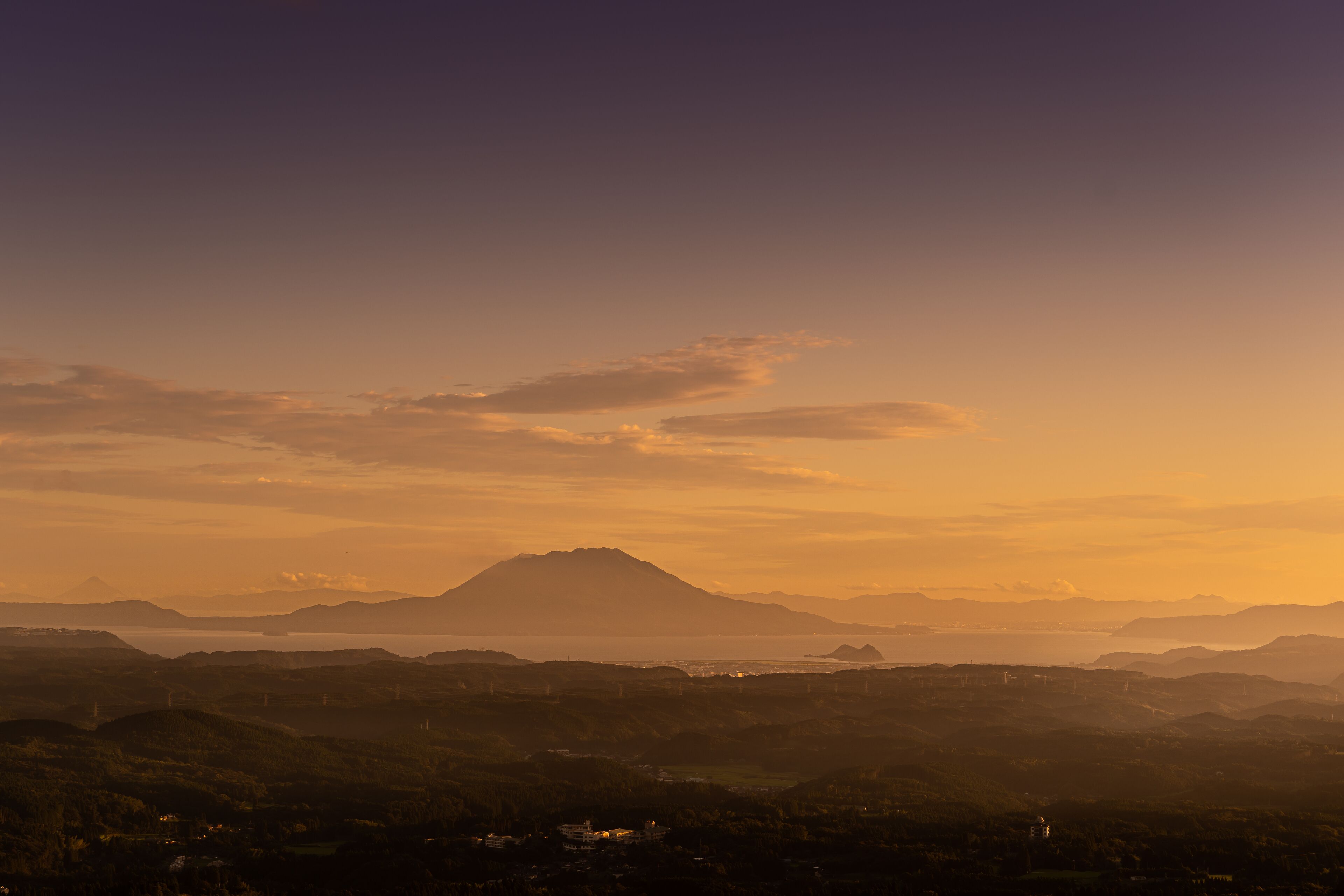 A panoramic view of a mountainous landscape with a distant mountain peak, a valley, and a body of water.