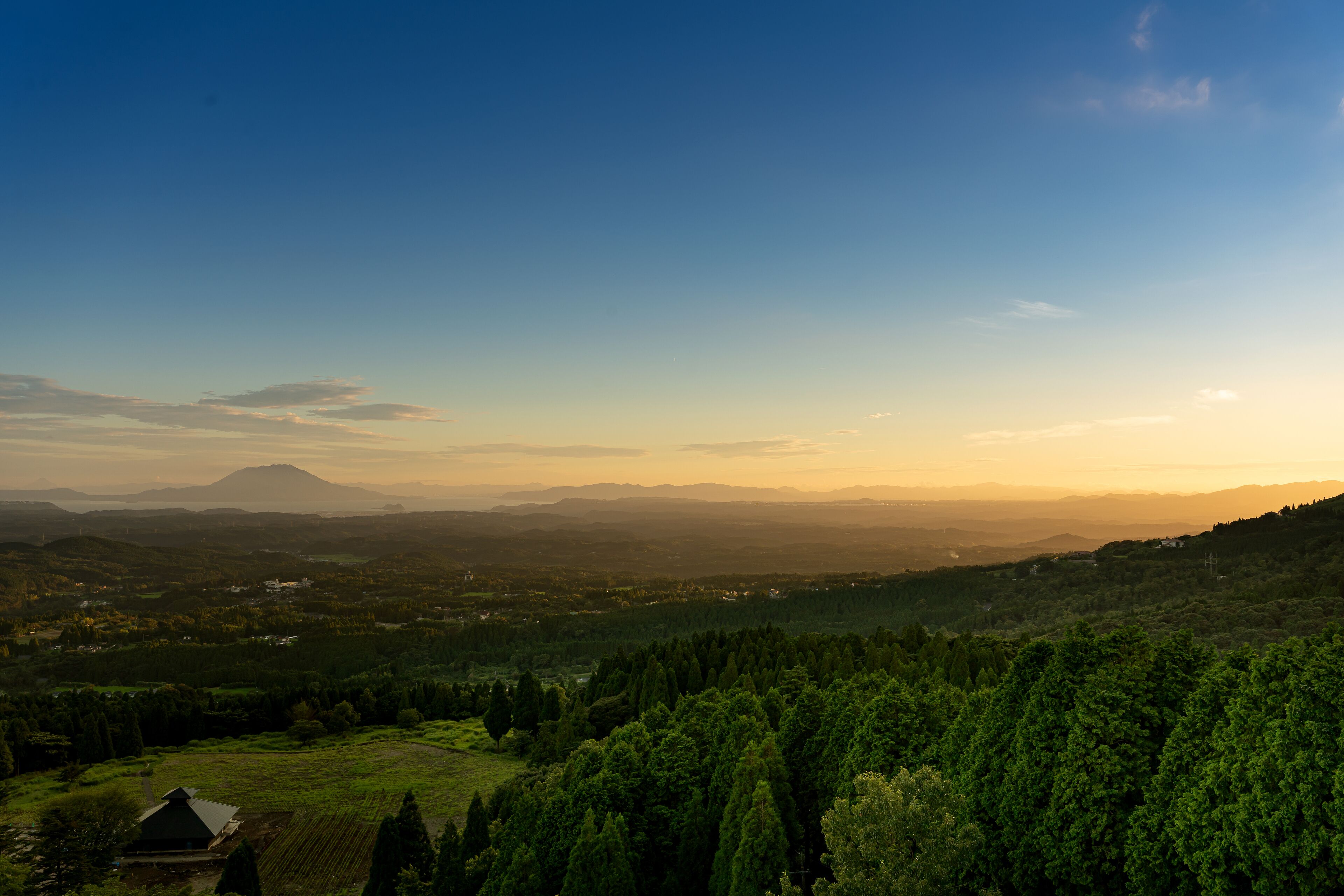 A panoramic view of a mountainous landscape with a small building in the foreground.