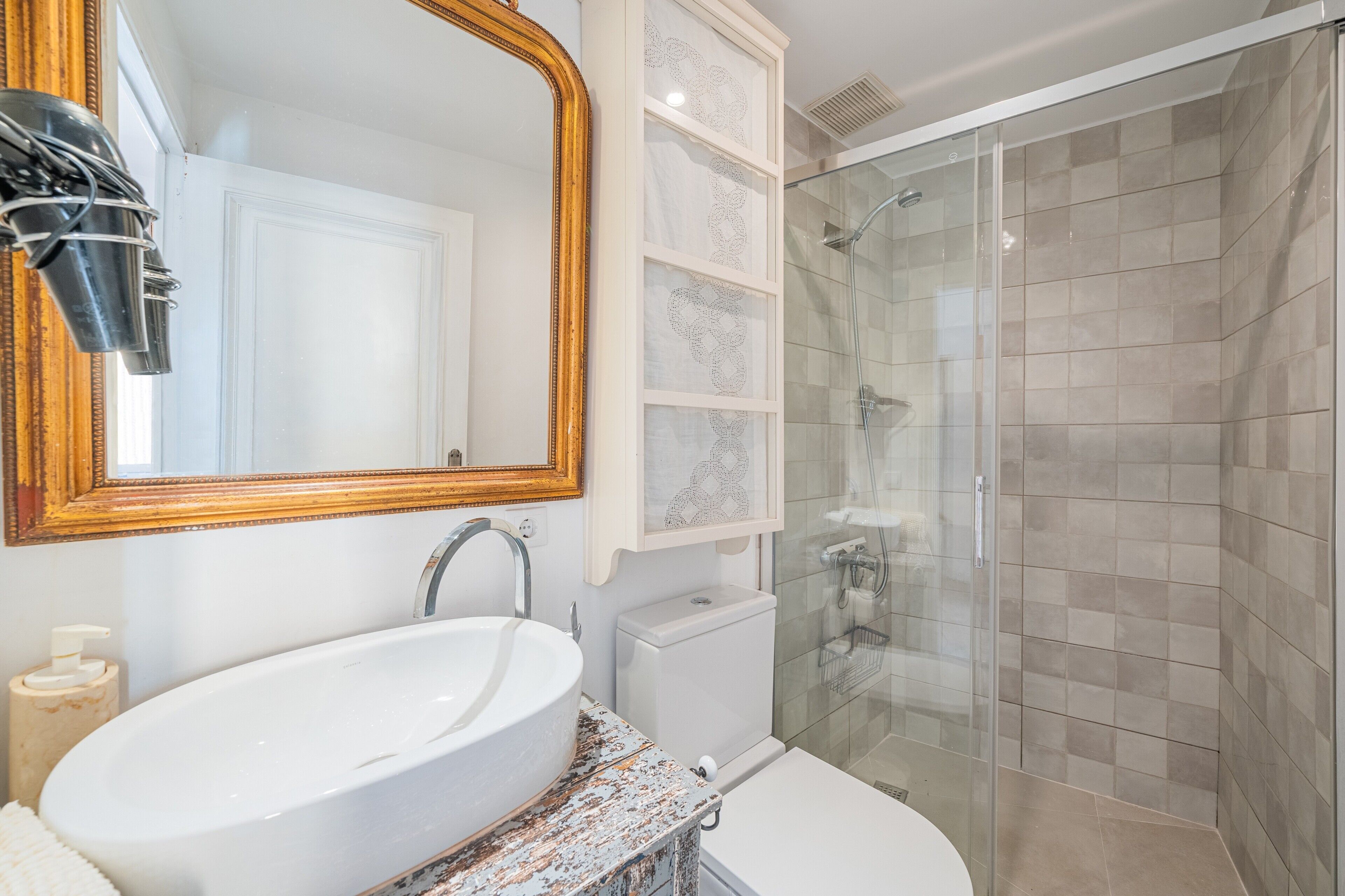 A bathroom with a large oval sink, a toilet, a glass shower enclosure, and a mirror with a wooden frame.