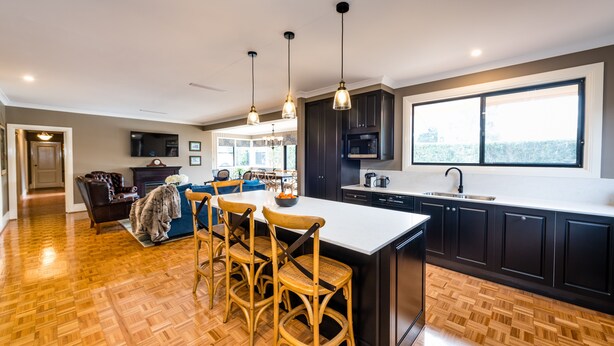 Une cuisine moderne avec des meubles de couleur sombre, un grand îlot central et des luminaires suspendus.