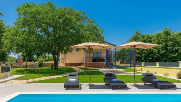 A swimming pool with lounge chairs and umbrellas, surrounded by a well-maintained lawn and trees. - Villa Aniva by Interhome (Rovinj/Žminj)