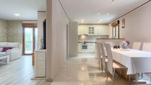A modern kitchen with white cabinets, a dining area with a table and chairs, and a living room with a sofa and a stone wall. - Villa Aniva by Interhome (Rovinj/Žminj)