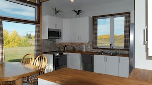 Une cuisine moderne avec des meubles blancs, un plan de travail en bois et une vue sur un champ verdoyant.