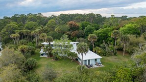 A large house surrounded by dense tropical vegetation, with a well-maintained lawn and a small patio area. - The Treehouse:Treeline View, Screened Porch, Private Balcony (Melbourne Village)