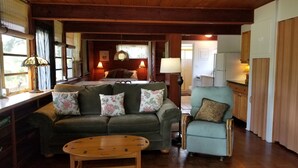 A cozy living room with a green sofa, a small round table, and a light blue armchair. - The Treehouse:Treeline View, Screened Porch, Private Balcony (Melbourne Village)