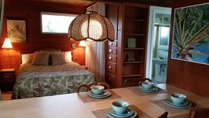 A cozy room with a bed, wooden dresser, and a dining table set with bowls. - The Treehouse:Treeline View, Screened Porch, Private Balcony (Melbourne Village)