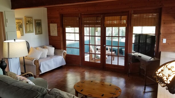 A cozy room with a wooden floor, a sofa, a small round table, and a TV. - The Treehouse:Treeline View, Screened Porch, Private Balcony (Melbourne Village)
