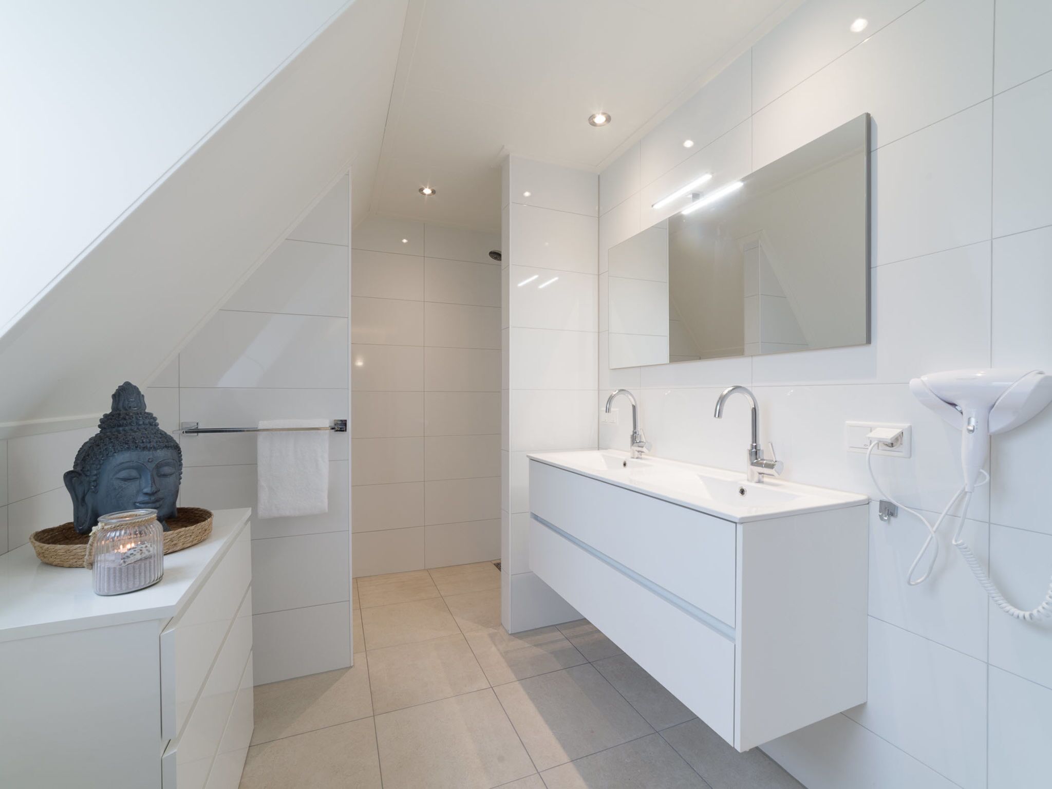 Une salle de bain moderne dotée d’une lucarne, d’un grand miroir, d’un meuble-lavabo à deux vasques et d’un sèche-cheveux.