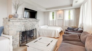 A room with a stone fireplace, a flat-screen TV, a bed, a sofa, and a coffee table.