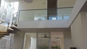 Ein modernes Interieur mit einem Glasbalkon, einer Treppe und Blick ins Freie.