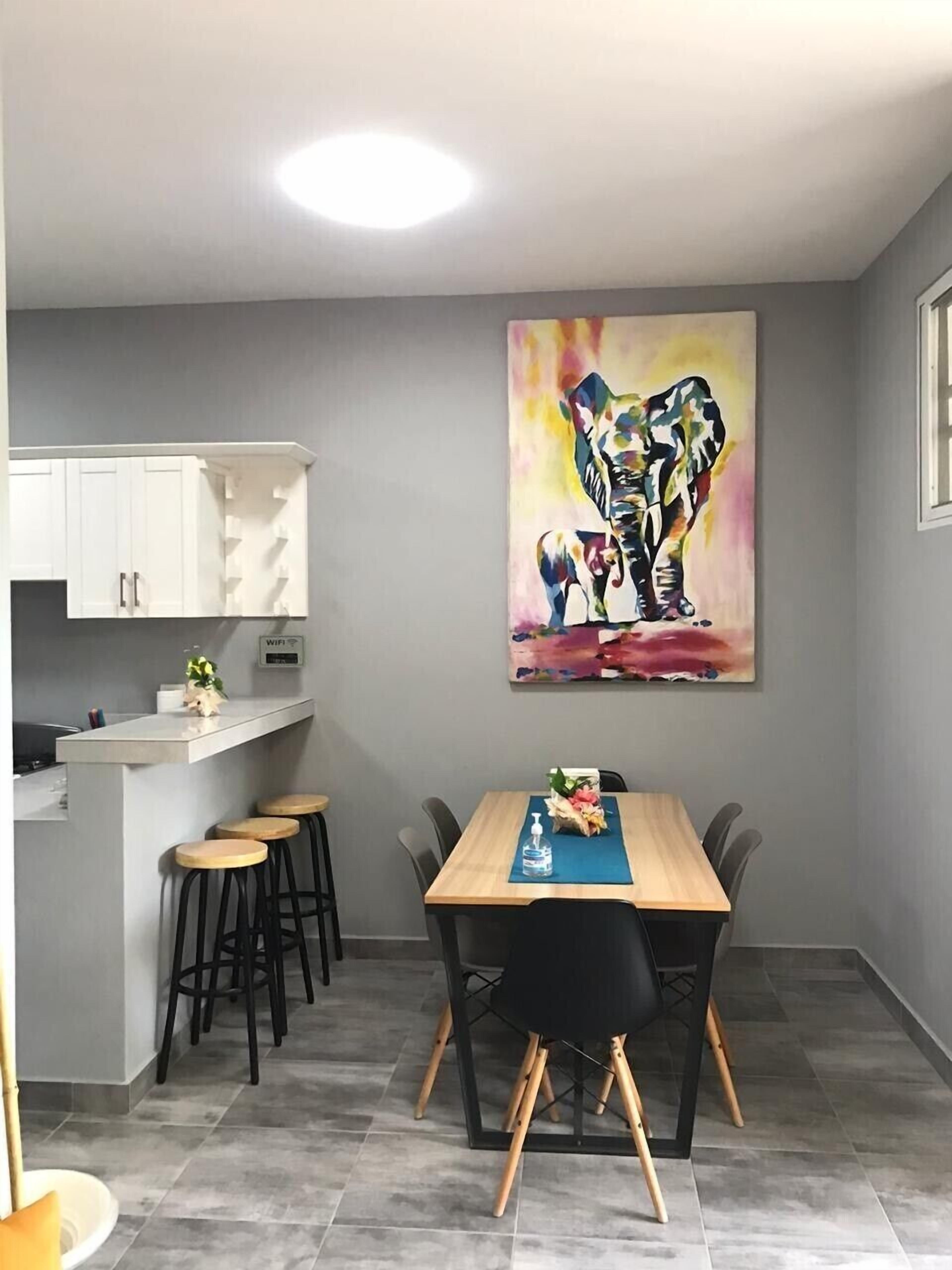 Una cocina moderna con armarios blancos, una mesa de comedor de madera con sillas negras y un cuadro abstracto y colorido en la pared.