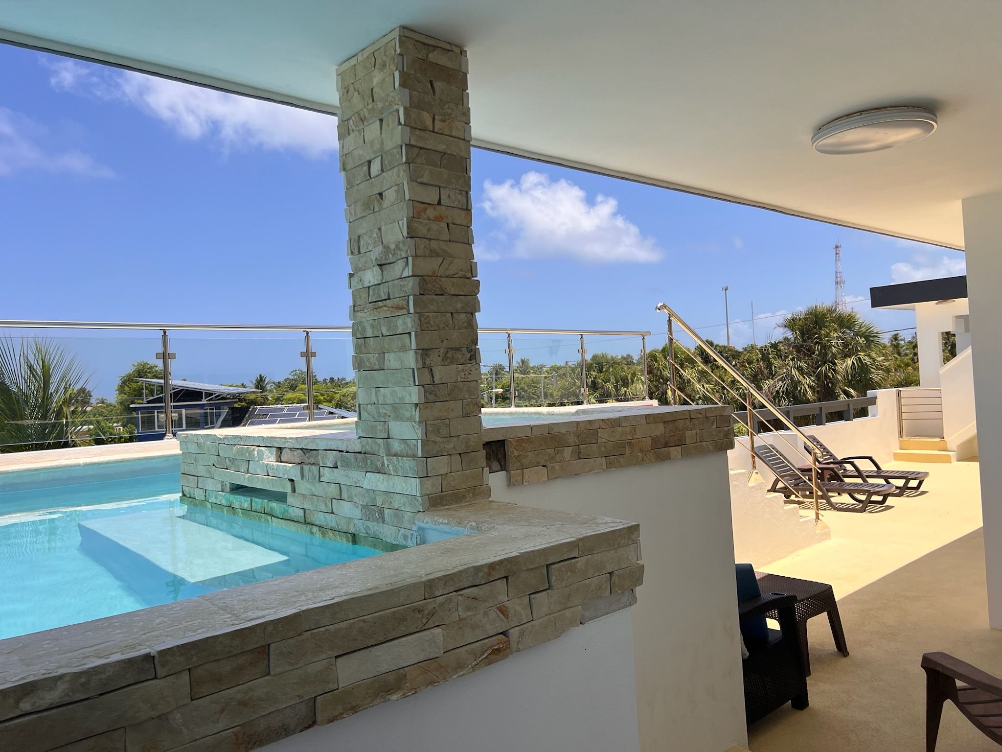 Una piscina con paredes de piedra, una terraza con sillones de descanso y una vista despejada del cielo.