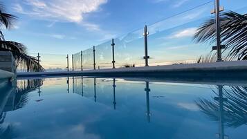 Una piscina cristalina con barrera de vidrio y palmeras al fondo.