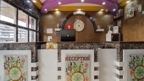 A reception area with a clock, a laptop, and a sign that reads "RECEPTION". - Hotel Mani International (Patna)
