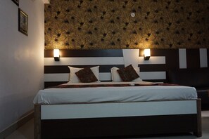 A hotel room with a large bed, black and white striped headboard, two wall-mounted lights, and a patterned wallpaper. - Hotel Mani International (Patna)