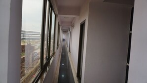 A narrow corridor with large windows on one side, leading to a door at the end. - Hotel Mani International (Patna)