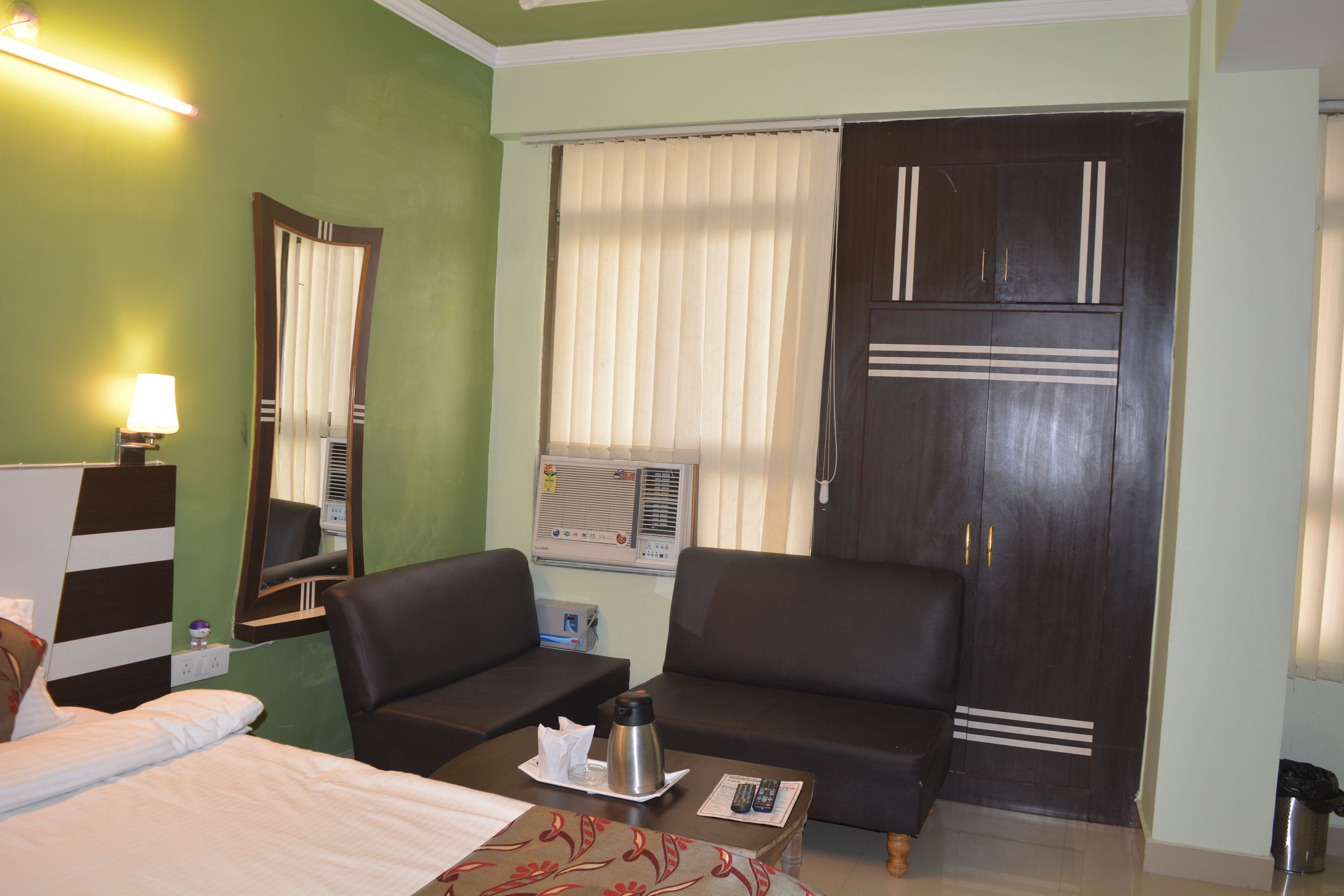 Habitación de hotel con una cama, dos sofás, una mesita de centro, un espejo, una ventana con cortinas y un armario.